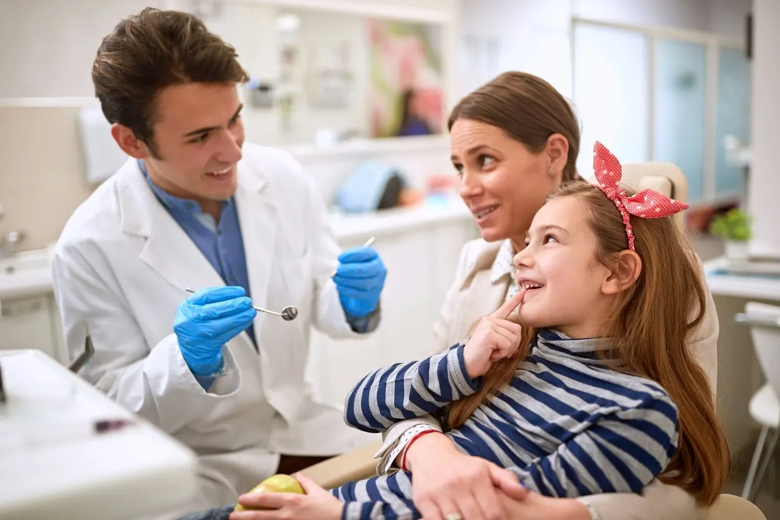 Dentist chatting warmly with a young patient and her mother